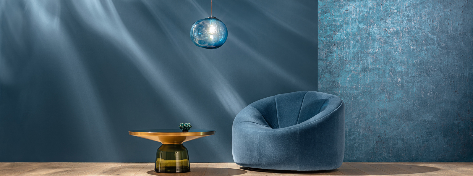Ein stilvolles Wohnzimmer mit einer runden blauen Sessellounge, einem goldenen Tisch mit grünem Akzent und einer eleganten blauen Pendelleuchte. Die Wände sind in einem tiefen Blau und einem schimmernden Aquamarin gehalten, und sanfte Lichtstrahlen fallen auf die Szene.